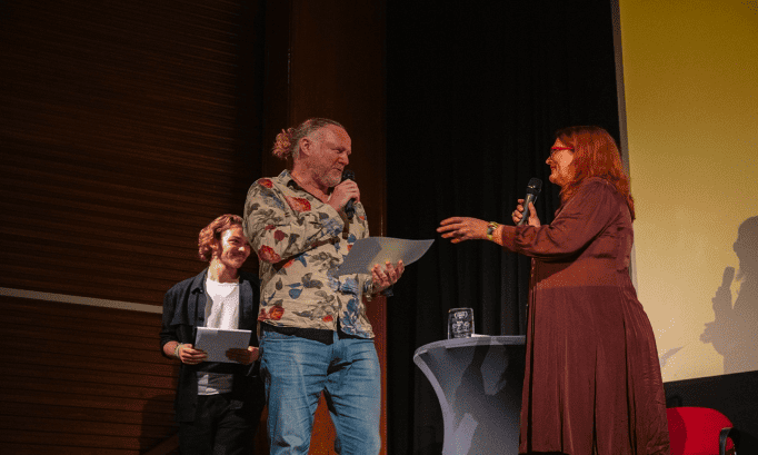 Cenu diváka v kategórii CINEDU Teens preberá od riaditeľky festivalu Ľudmily Cvikovej scenárista filmu John Chambers, vpravo moderátor večera herec Oliver Asztalos